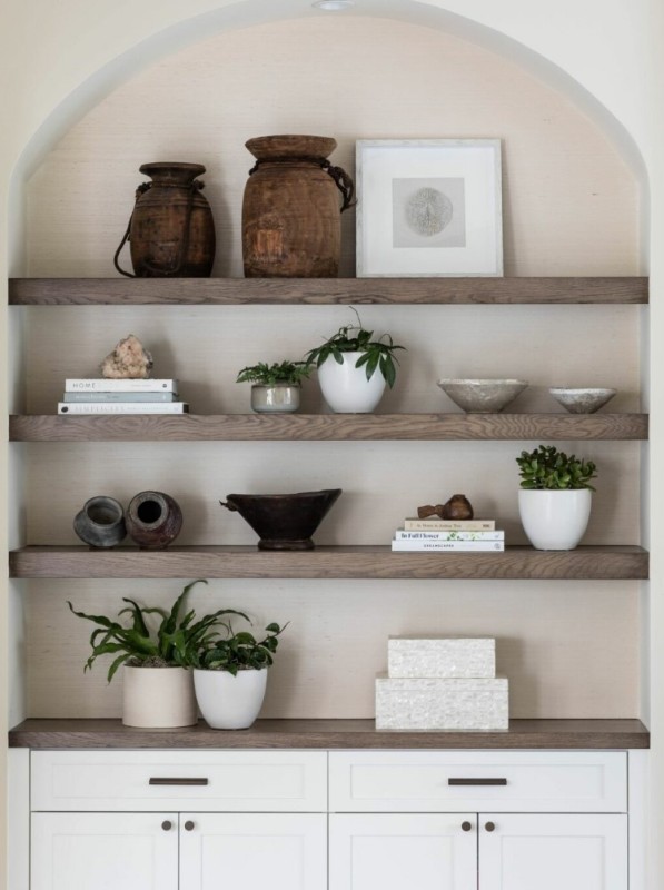 a large arched niche with stained shelves and a built in storage unit, potted plants, vases and books is a cool way to add interest