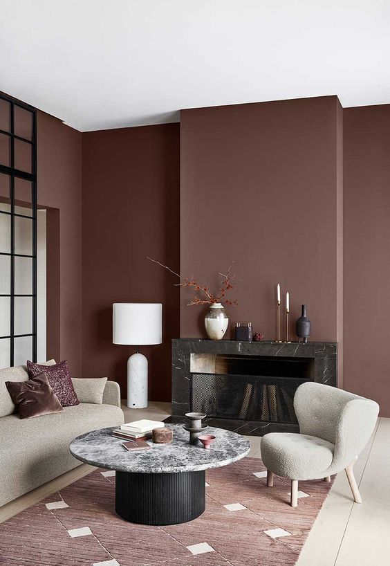 a refined and chic living room with chocolate brown walls, a built-in black fireplace, neutral furniture, a black and white table and a burgundy rug