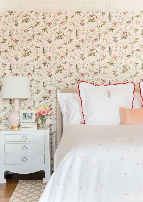 a cozy vintage-inspired bedroom with a floral wallpaper wall, polka dot bedding, vintage-inspired furniture and a blush lamp