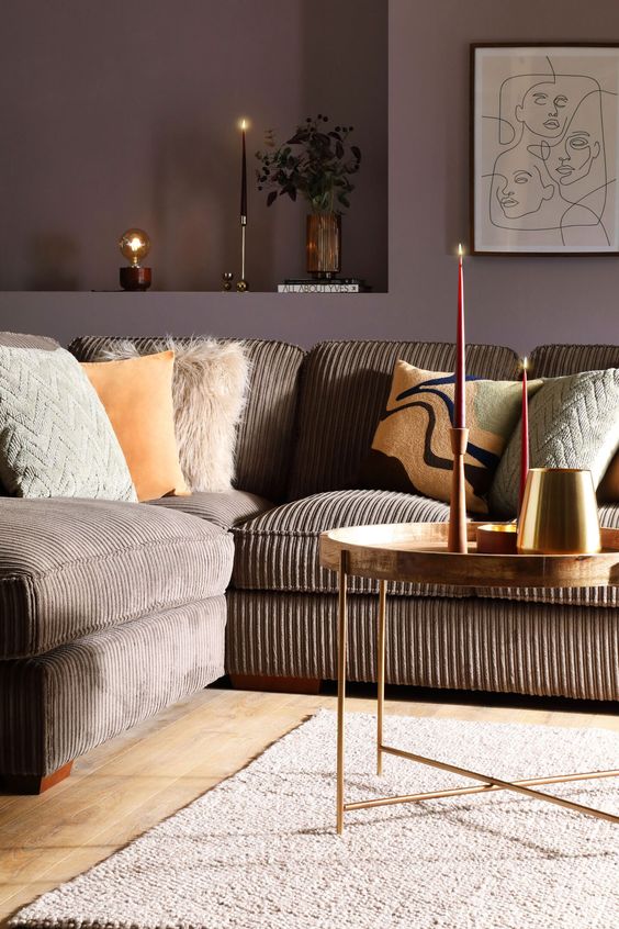 an exquisite and chic living room with taupe walls, a brown sofa with various pillows, a neutral rug and tall and thin candles
