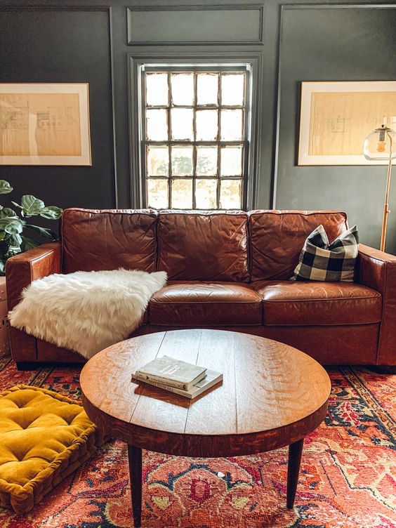 a welcoming and cozy living room with grey grene walls, a brown leather sofa, a mustard cushion, a red printed rug
