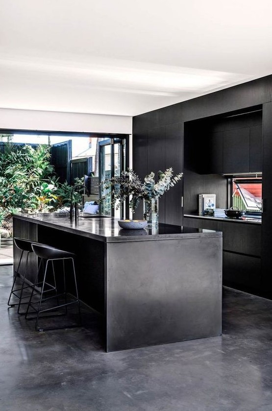 a contemporary moody kitchen with sleek black cabinetry, a kitchen island, a glazed wall with an entrance to a courtyard