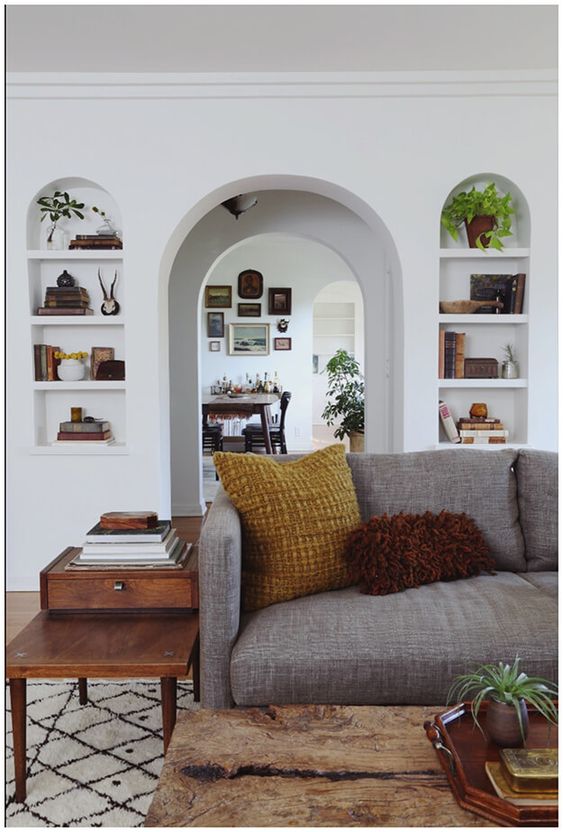 a neutral living room with an arched doorway, arched niches with shelves to display books, potted plants and decor