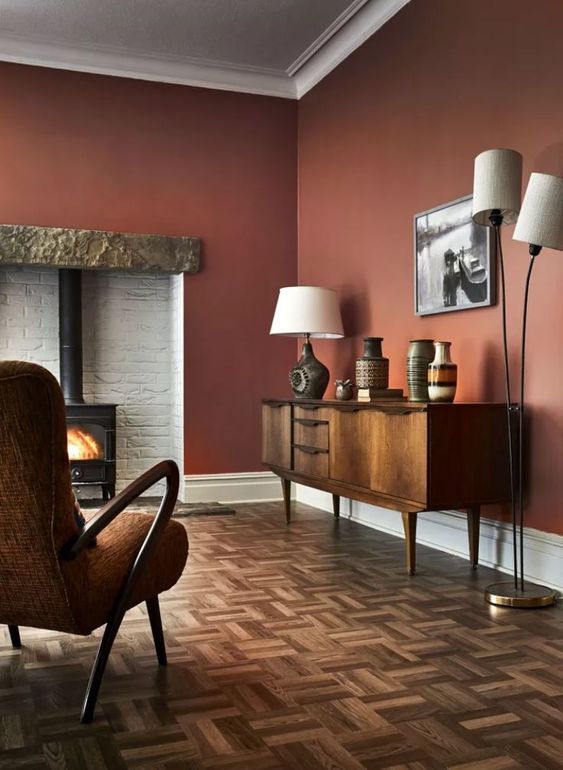 a rich-colored living room with burgundy walls, a hearth, a vintage credenza, a floor and table lamp