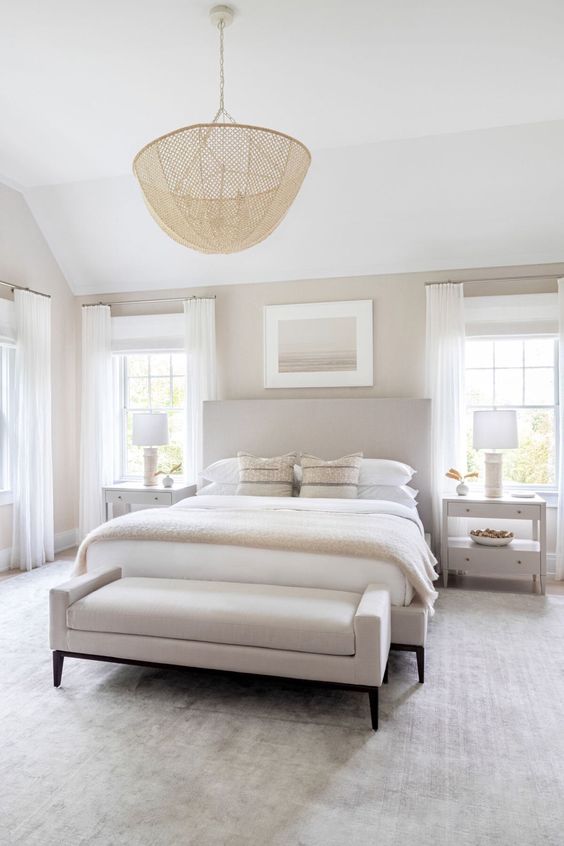 a neutral modernized yet classic bedroom with a bed with an extended headboard and a matching upholstered bench, a woven pendant lamp