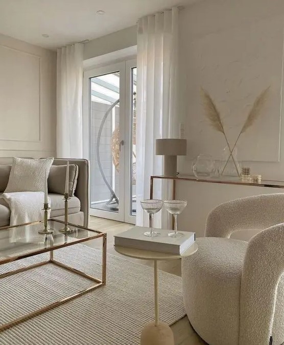 a refined contemporary living room with paneling, a glass console table, neutral furniture, a duo of side tables and neutral textiles