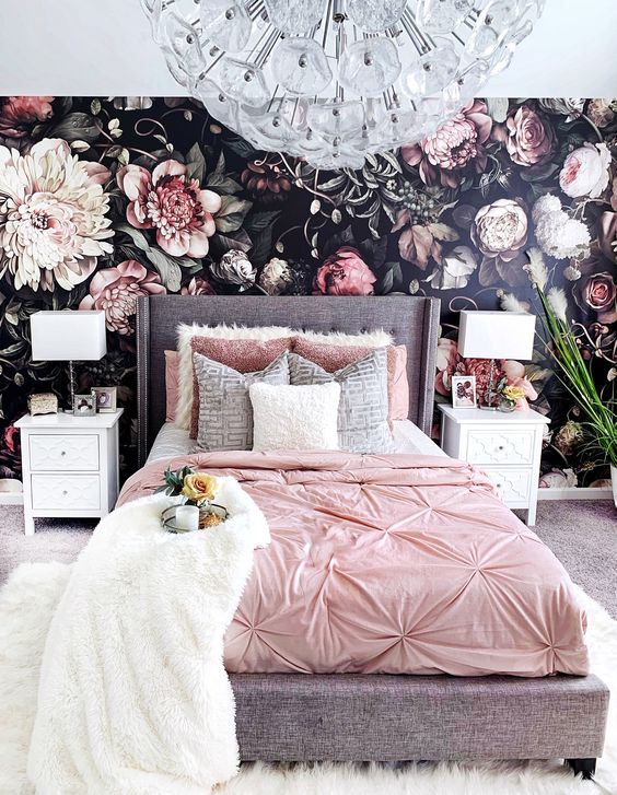 a realistic floral wallpaper wall, a grey bed with pink bedding, white inlay nightstands and a chic crystal flower chandelier