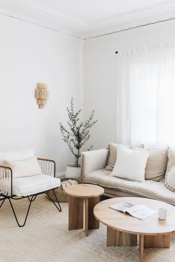a welcoming neutral living room with a neutral sofa and a black metal chair with white upholstery, round coffee tables and a potted plant