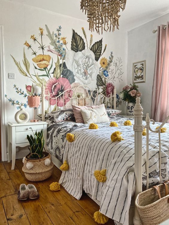 a teenage bedroom with a floral wall, a white metal bed, printed bedding, blush curtains, a cool chandelier and a plant in a basket