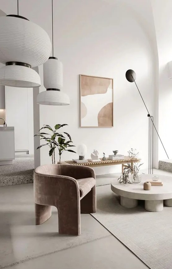 an exquisite neutral living room with a wooden bench used for displaying, a low round coffee table, a dusty pink chair and pendant lamps