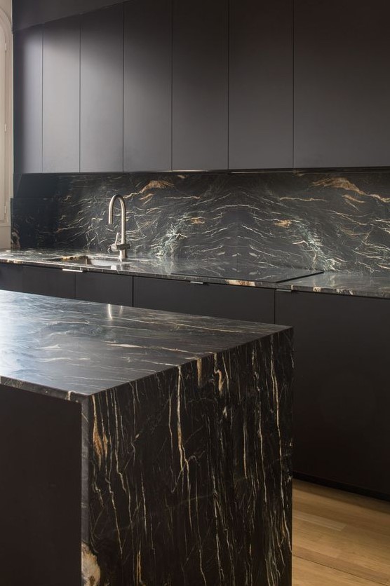 a minimalist black kitchen with sleek cabinets, black marble countertops and a backsplash and neutral fixtures
