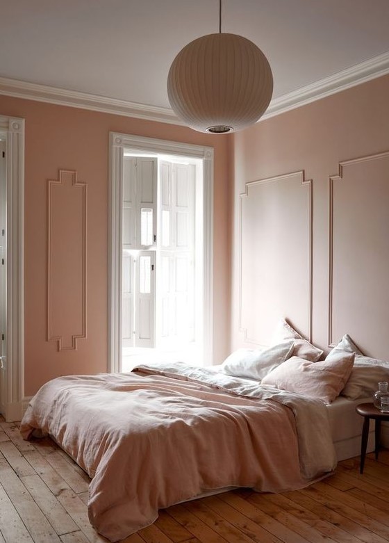 a refined vintage-inspired bedorom with blush molding walls, blush and white bedding, a wooden floor and a paper lamp