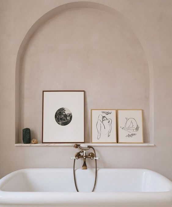 a warm colored bathroom with limewashed walls, a tub with vintage fixtures and an arched niche with a ledge to show off some artwork