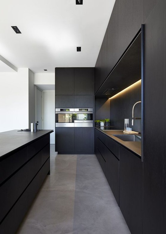 a minimalist black kitchen with sleek cabinets, built-in lights, a large kitchen island and built-in appliances