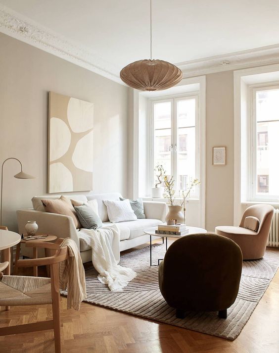a warm-colored neutral living room with greige walls, a creamy sofa with neutral pillows, a tan chair and a side table