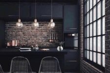 20 a moody kitchen with black cabinetry, brick walls for a strong industrial feel, metal chairs, round pendant lamps