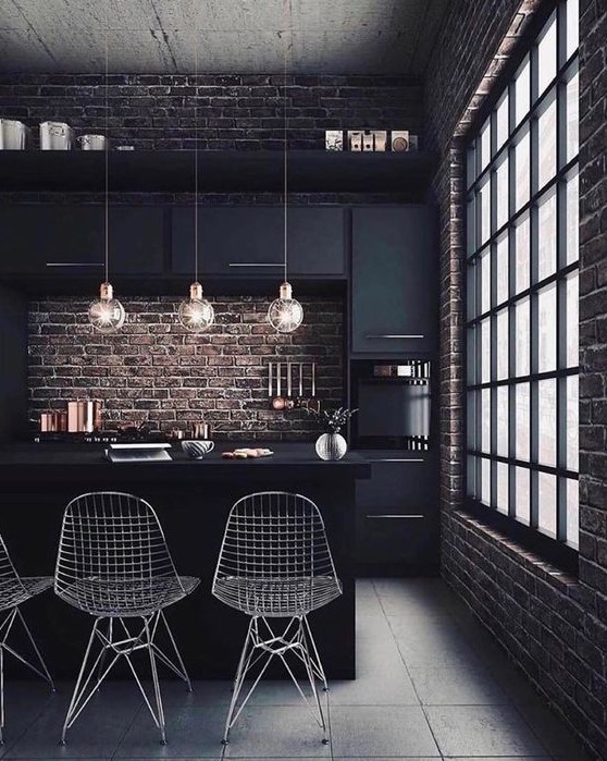 a moody kitchen with black cabinetry, brick walls for a strong industrial feel, metal chairs, round pendant lamps