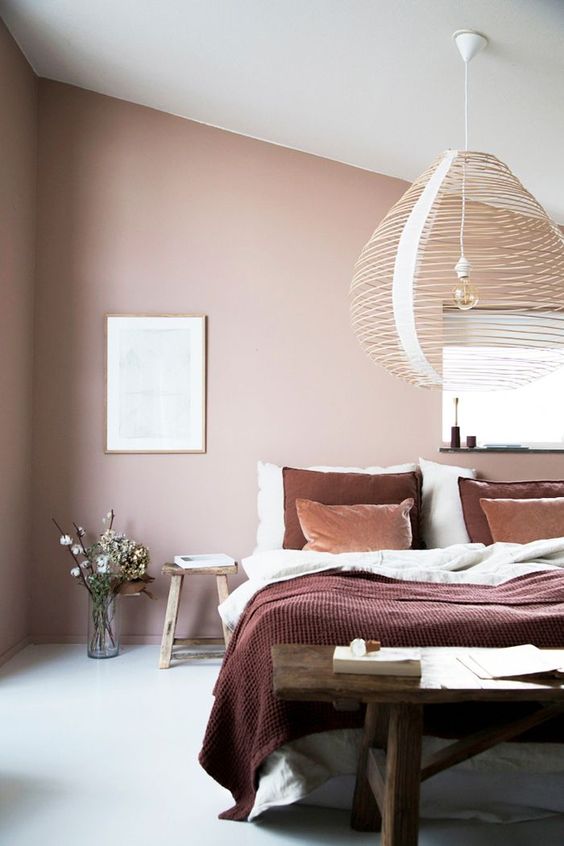 a beautiful attic bedroom with blush walls, a bed with contrasting bedding, a dark-stained wooden bench and a woven pendant lamp