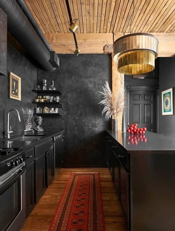 a moody yet bold kitchen with black cabinetry, black walls, a wooden ceiling, a gold chandelier and pampas grass in a vase