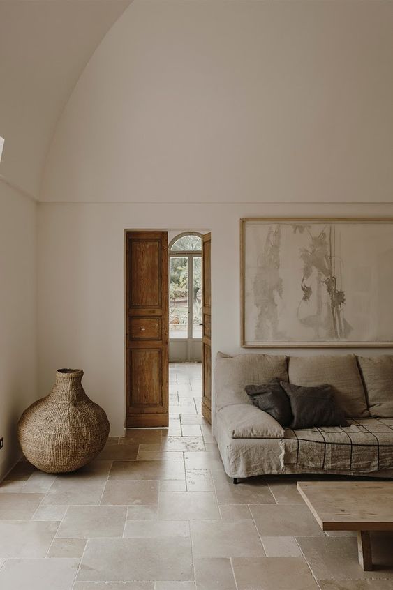 a neutral minimalist living room with a Mediterranean feel, with a grey sofa and black pillows, a low coffee table, a large woven vase