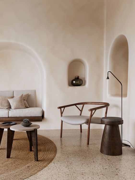 a minimalist Mediterranean living room with plaster walls and niches, a built-in sofa in one of them, a neutral chair and some side tables