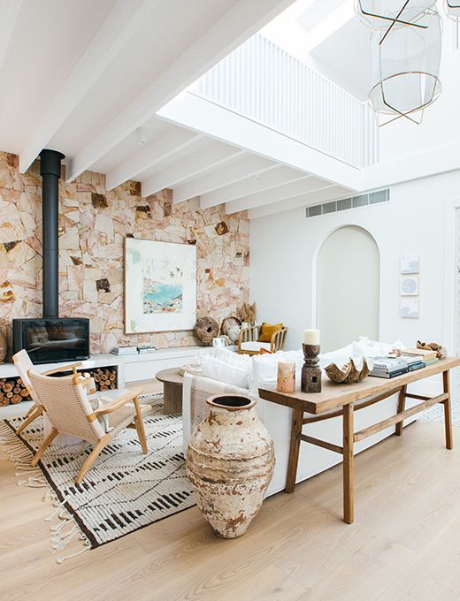a neutral minimalist living room with a Mediterranean touch, with a white sofa, neutral woven chairs, a hearth and a catchy accent wall