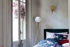 27 a chic bedroom with concrete walls, a black bed with pink, navy and black floral bedding, chic gilded lamps and a stack of books