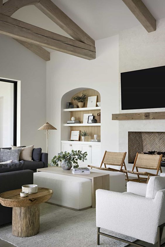 a neutral Mediterranean living room with a niche with shelves and built-in storage units, a fireplace, a charcoal grey sofa and creamy chairs and an ottoman