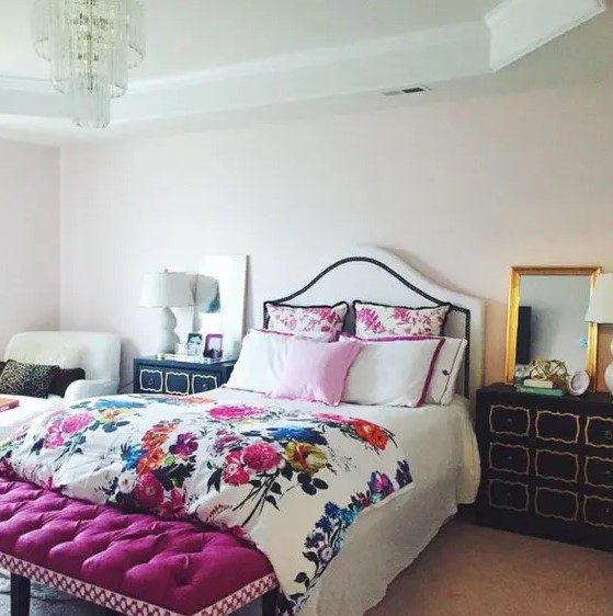 a glam bedroom with an upholstered bed and floral bedding, a fuchsia upholstered bench, black dressers and a chair