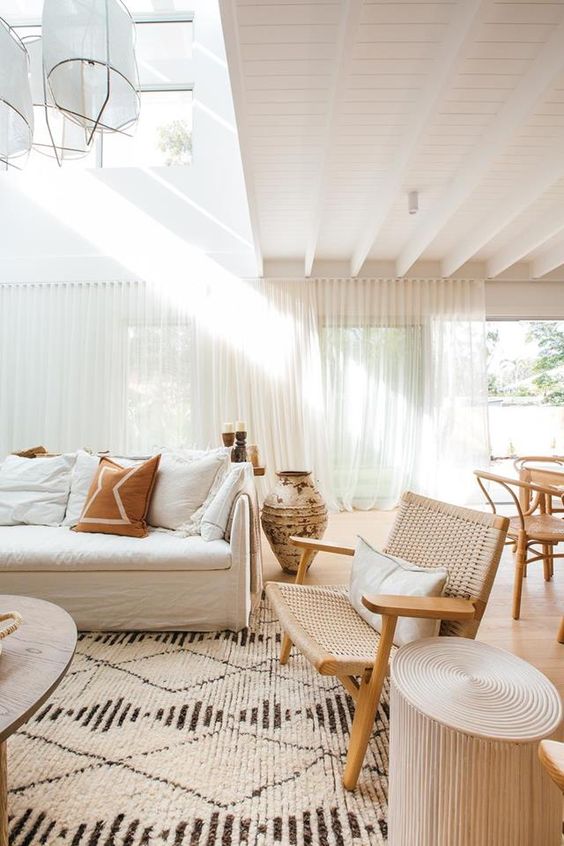 a minimal Mediterranean living room with a lot of natural light, a creamy sofa, a woven chair, side tables and a coffee table