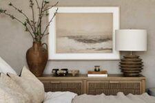 28 a neutral bedroom with grey limewashed walls, a bed with neutral textural bedding, a wooden credenza and a lamp with a wooden base