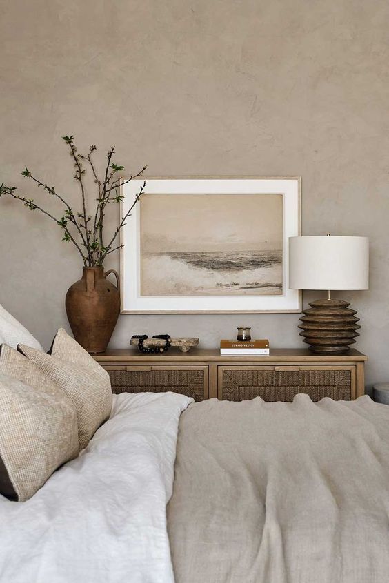 a neutral bedroom with grey limewashed walls, a bed with neutral textural bedding, a wooden credenza and a lamp with a wooden base