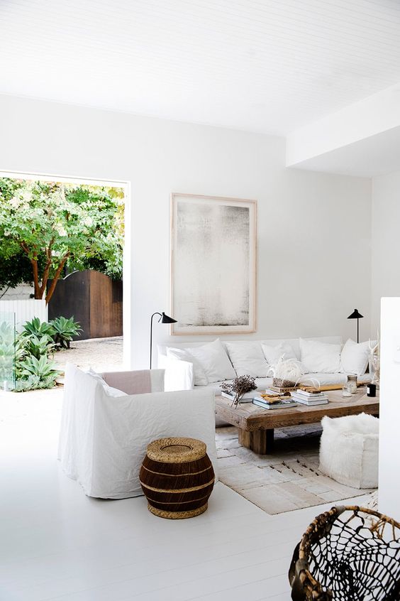 a minimal Mediterranean living room with a white sofa, chairs and poufs, a low rough wood coffee table and a woven side table