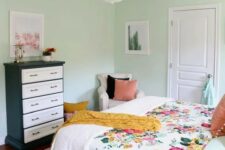 29 a mint-colored bedroom with a bed and floral bedding, a black and white dresser, a neutral chair and a chandelier