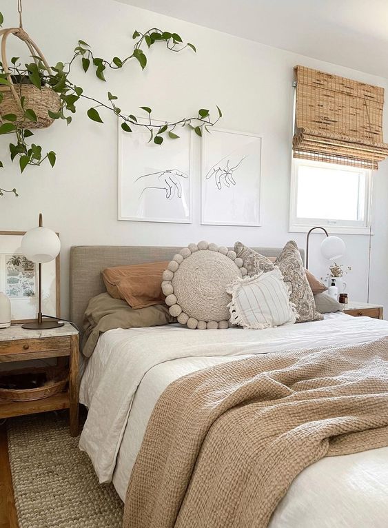 a neutral bedroom with a boho feel, an upholstered bed with textural bedding, a woven rug, wooden nightstands and greenery