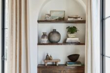 29 an awkward nook turned into a catchy part of decor, with an arched niche, a dark-stained cabinet and shelves, with some decor on display