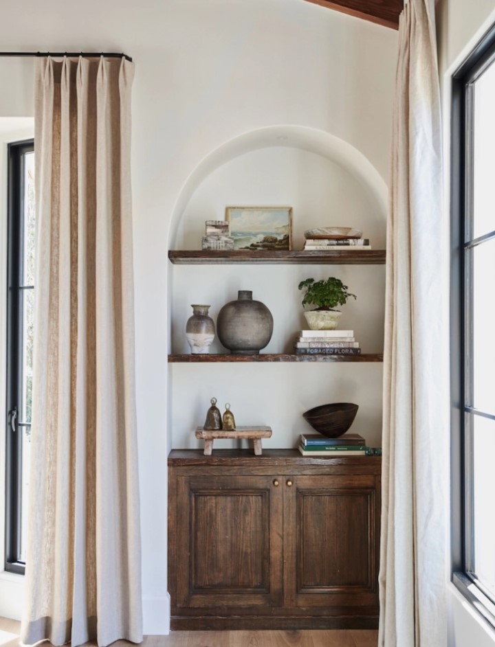 an awkward nook turned into a catchy part of decor, with an arched niche, a dark stained cabinet and shelves, with some decor on display