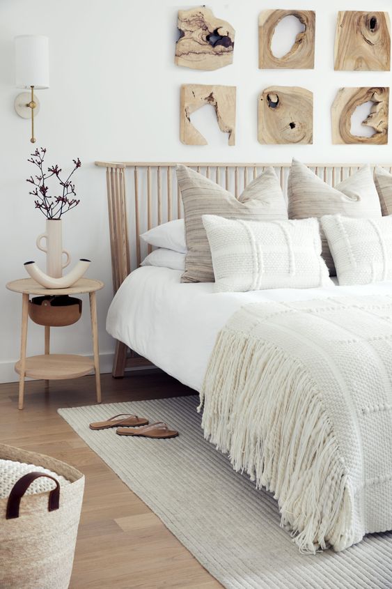 a neutral bedroom with a curved wooden slat headboard and textural and woven bedding, pieces of wood on the wall and a nightstand with unique lamps