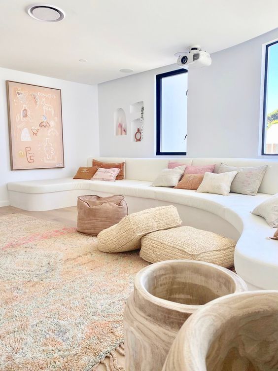 a chic minimal Mediterranean living room with a creamy curved sofa, neutral pillows, woven poufs and cushions, a large artwork