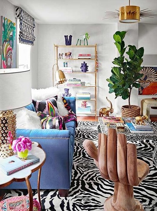 a maximalist living room with a blue sofa, a whimsy chair, colorful rugs and pillows and a bold statement plant in a basket