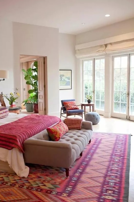 a bold bedroom with a colorful printed rug, a bold blanket and pillows that make this space super colorful