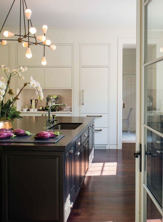 a chic neutral kitchen with a niche tea station, a large black kitchen island, a lovely chandelier and some orchids