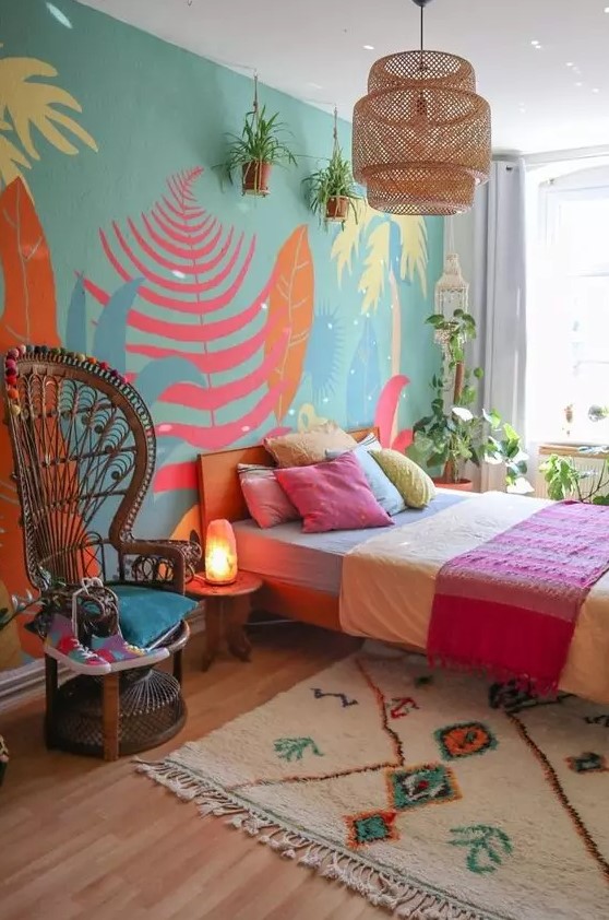 a bright boho sleeping space with a wall mural, a bed with colorful bedding and a rug, a woven pendant lamp and a papasan chair