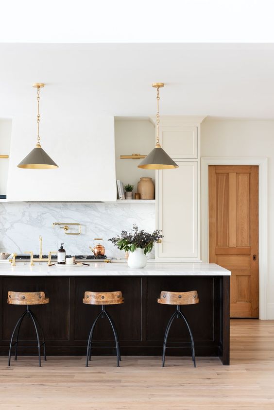 a chic white kitchen with shaker cabinets, open shelves, a large hood, a black kitchen island with a white stone countertop