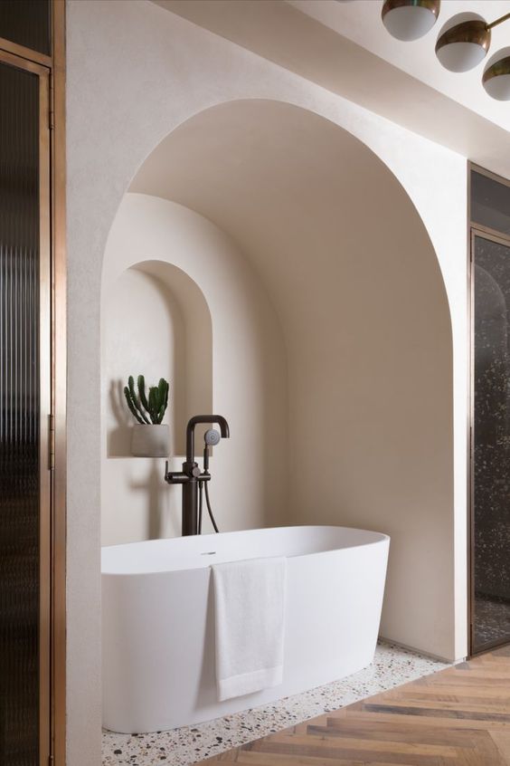 a neutral bathroom with an oval tub placed in a niche, with an additional niche with a potted plant looks jaw dropping