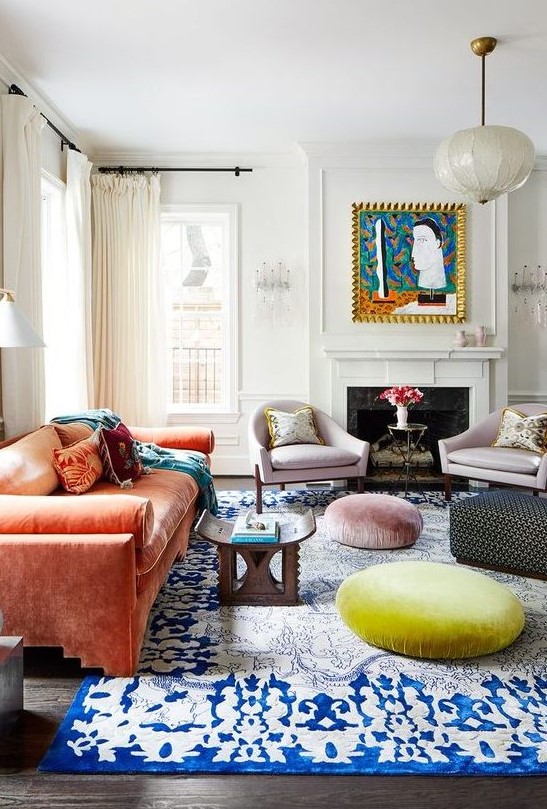 a maximalist living room with a coral sofa, a bold blue rug, pastel ottomans, lilac chairs and a bold artwork