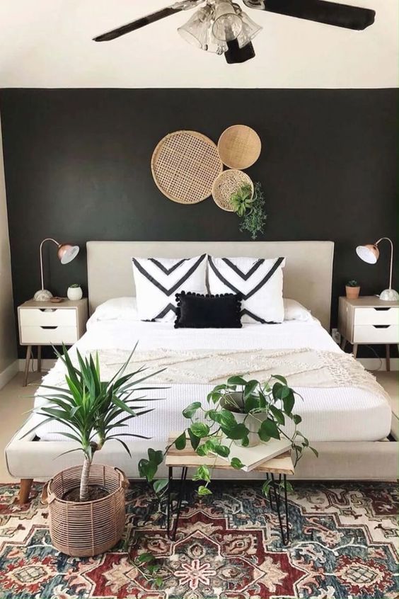 a stylish boho bedroom with a black accent wall, a neutral bed, printed pillows and a printed rug, potted greenery