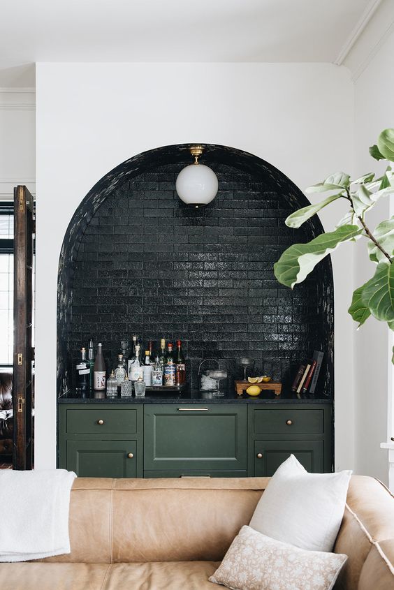 an arched niche clad with dark green brick, with a lamp and a some bar done with green cabinets is a fantastic idea