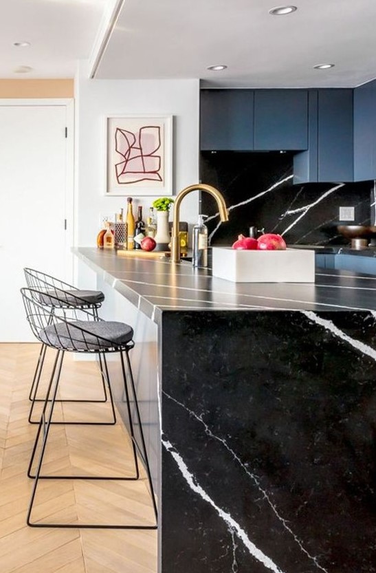 a blue kitchen with a black marble backsplash and a waterfall countertop plus touches of gold for a chic look