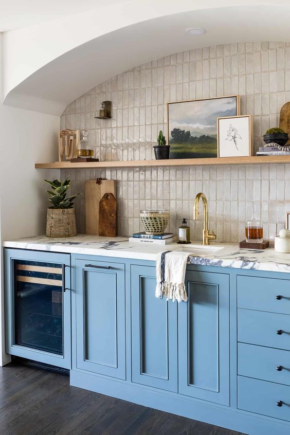 an arched niche clad with mother of pearl skinny tiles, with an open shelf for displaying art and decor and blue cabinetry